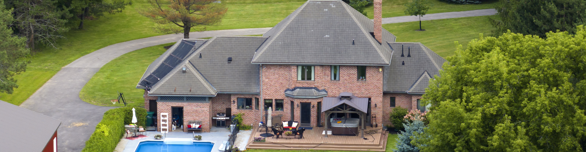Aerial view of a large brick residential home with garden, pool, and outdoor entertainment area